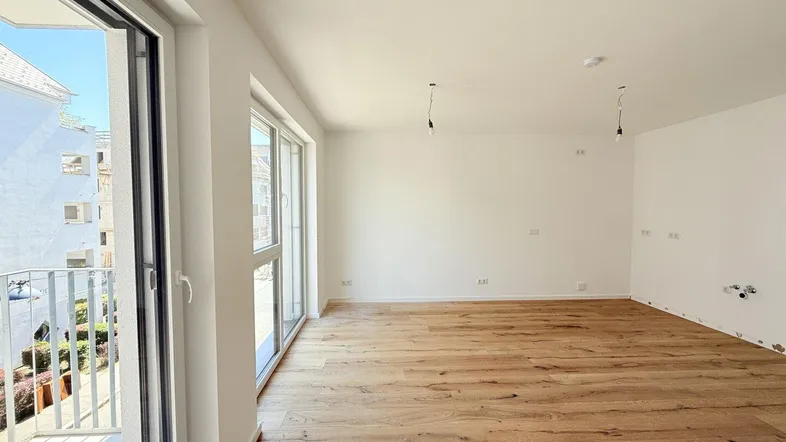Helles, leeres Wohnzimmer mit Holzboden und Zugang zu einem Balkon, bereit zur individuellen Gestaltung.