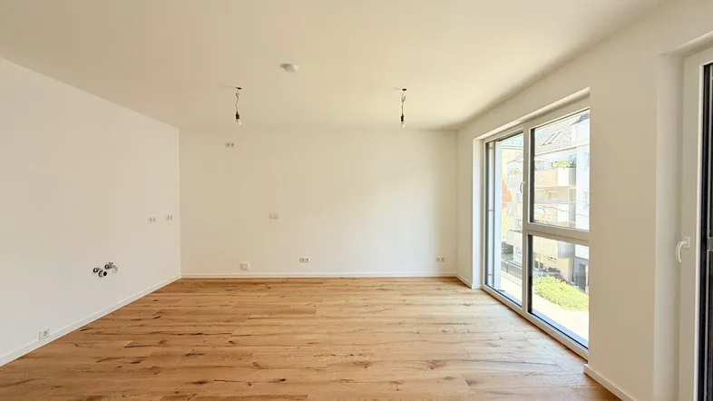 Helles, leeres Wohnzimmer mit neuem Holzboden und großen Fenstern, die viel Tageslicht hereinlassen.