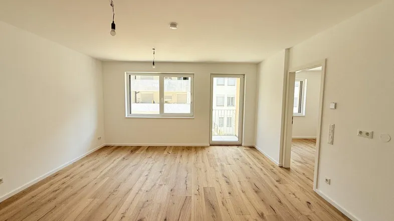Helles, leeres Zimmer mit modernem Holzboden und Zugang zu einem Balkon, ideal als Wohnbereich.