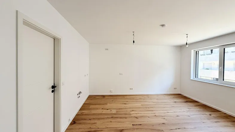 Helles, leeres Zimmer mit neuem Holzboden und weißen Wänden, bereit zur individuellen Gestaltung.