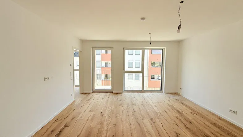 Helles, leeres Zimmer mit neuem Holzboden und großen Fenstern, bereit zur individuellen Gestaltung.