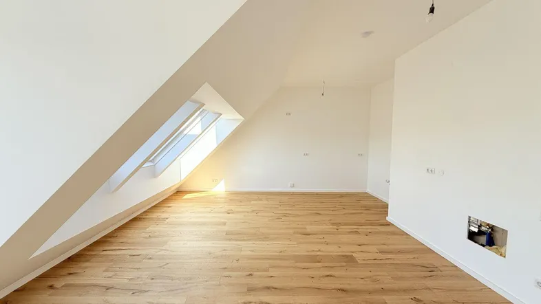 Helles Dachzimmer mit Holzboden und schrägen Wänden, durch Dachfenster gut belichtet.