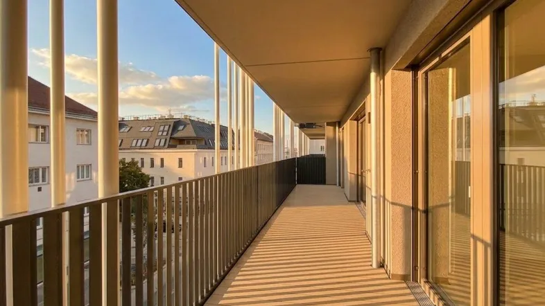 Langer Balkon mit modernem Geländer und Blick auf die umliegenden Gebäude bei Sonnenuntergang.