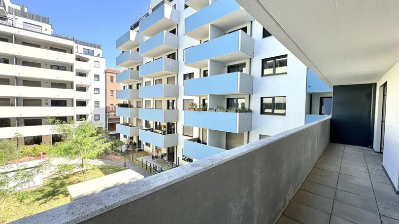 Blick von einem Balkon auf ein modernes Apartmentgebäude mit blauen Balkonen und einem grünen Innenhof.