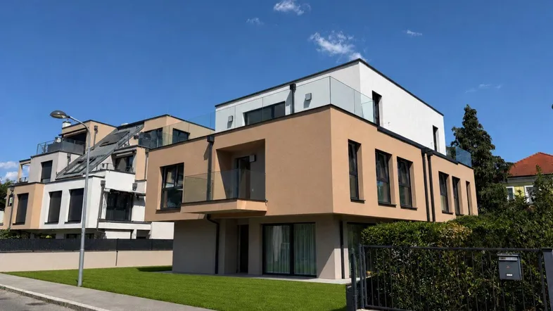 Moderne Wohnanlage mit Flachdach, Balkonen und gepflegtem Vorgarten unter blauem Himmel.