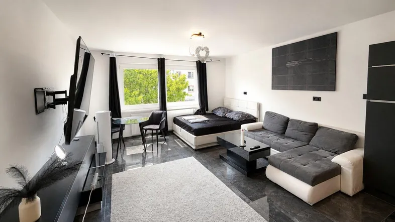 Moderner Wohn- und Schlafbereich mit dunklen Fliesen, bequemer Couch und großem Fenster.