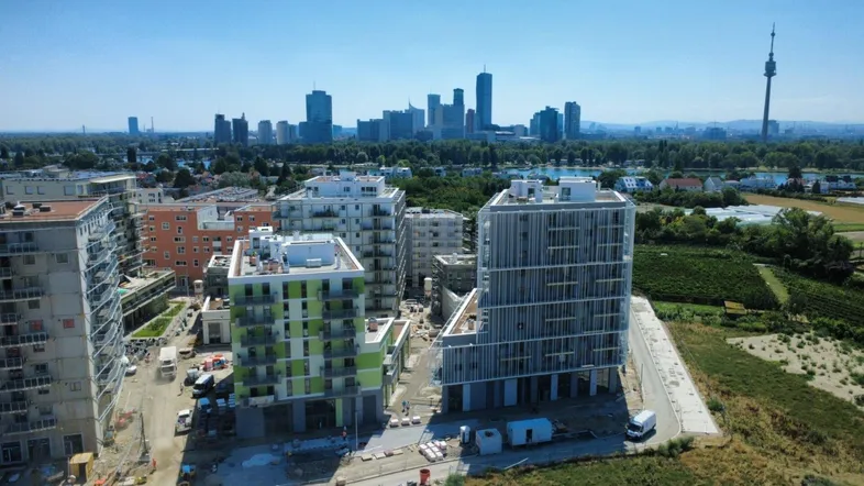 Luftaufnahme einer modernen Wohnsiedlung im Bau mit Blick auf die Wiener Skyline und Donau.