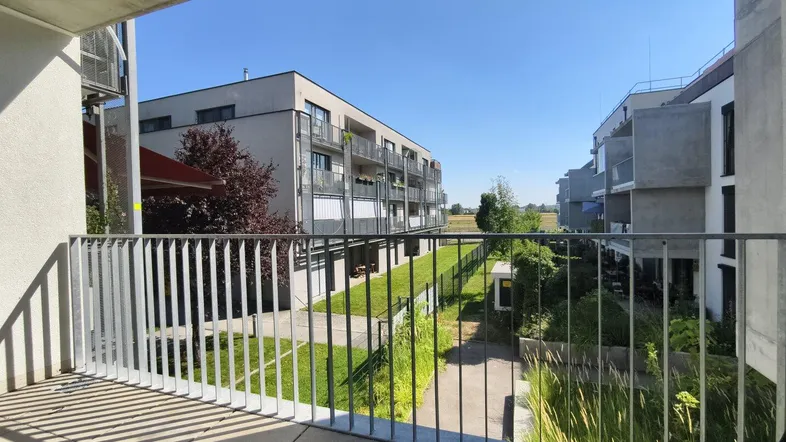 Blick vom Balkon auf die umliegenden modernen Gebäude und Grünflächen unter blauem Himmel.