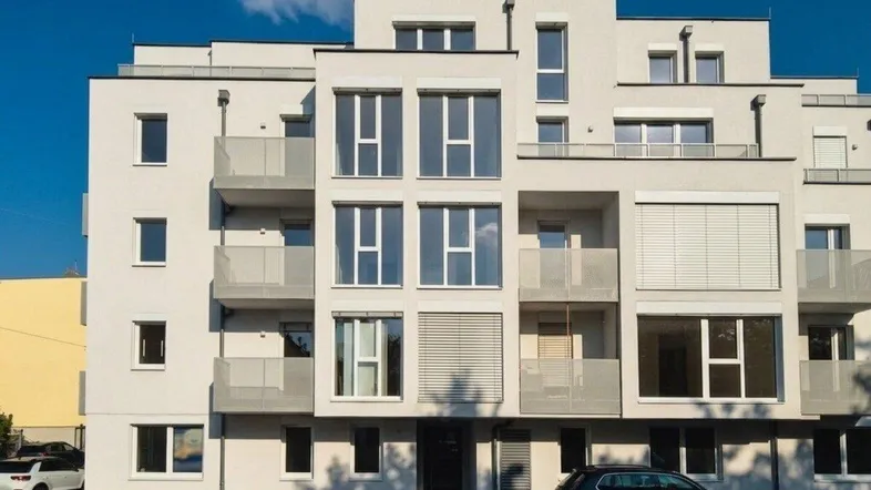 Moderne Wohnhausfassade in Weiß mit großen Fenstern und Balkonen unter blauem Himmel.