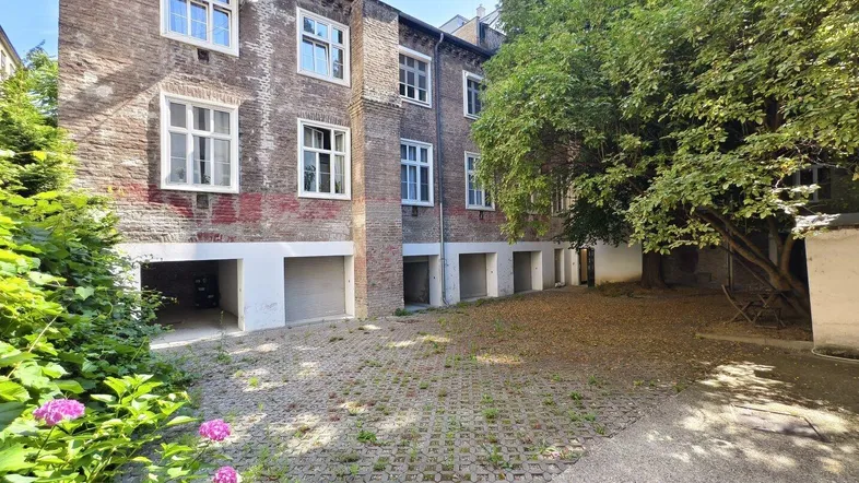 Backsteingebäude mit mehreren Fenstern und Garagen im Erdgeschoss, umgeben von einem begrünten Innenhof.