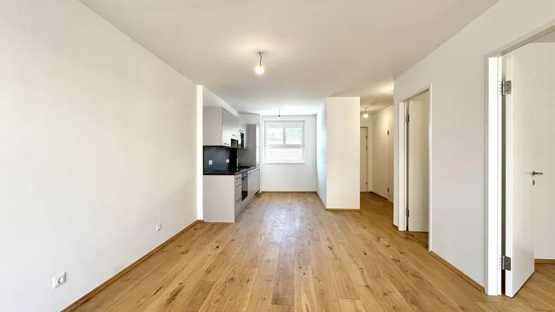Heller, offener Wohnbereich mit integrierter Küche und hochwertigem Holzfußboden in Neubauqualität.