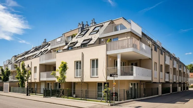 Modernes Mehrfamilienhaus mit mehreren Balkonen und Dachfenstern unter blauem Himmel.