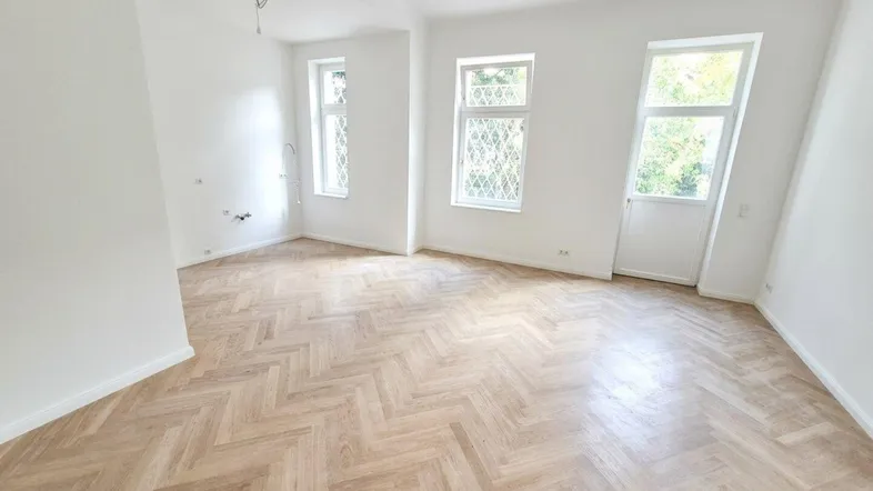 Helles Zimmer mit Fischgrätparkett und mehreren Fenstern, ideal als Wohn- oder Schlafzimmer.