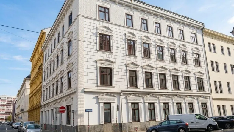 Weißes Mehrfamilienhaus mit klassischer Fassade und braunen Fenstern an einer Stadtstraße.