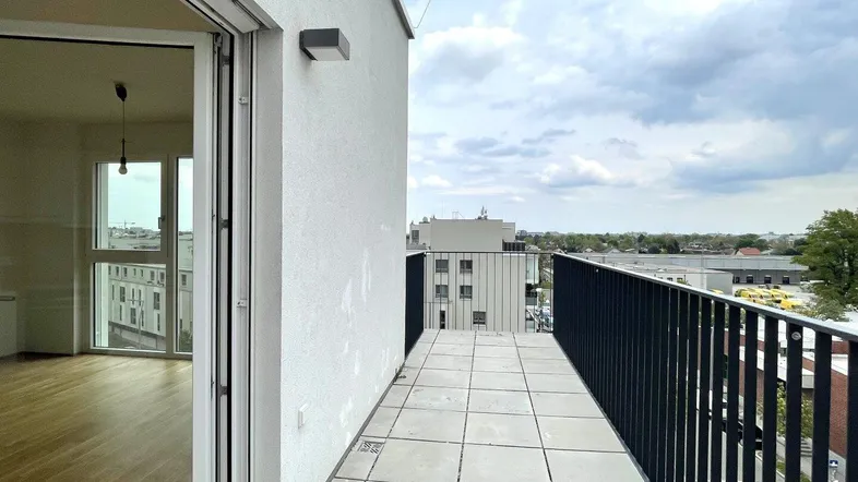 Geräumiger Balkon mit Fliesenboden und Blick auf die umliegende Stadtlandschaft und andere Gebäude.