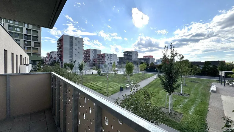 Balkon mit Blick auf eine moderne Wohnsiedlung und grüne Parkanlagen unter blauem Himmel.