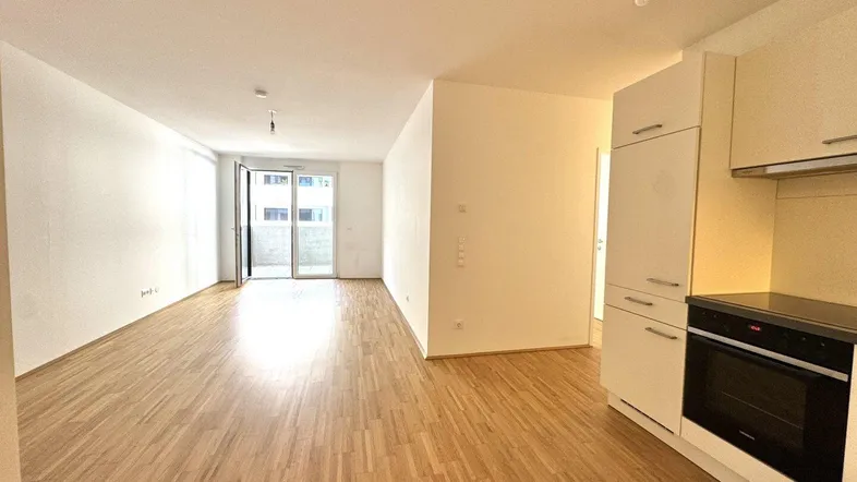 Heller, offener Wohn- und Essbereich mit Parkettboden und integrierter Küchenzeile, mit Zugang zum Balkon.