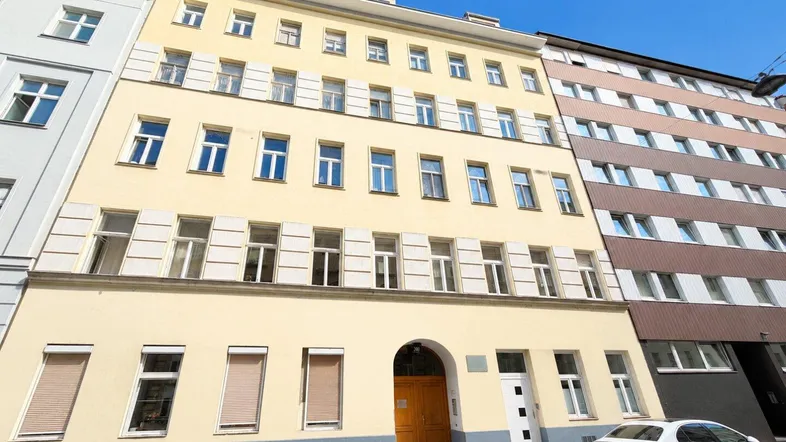 Klassisches Mehrfamilienhaus mit gelber Fassade und vielen Fenstern in städtischer Umgebung.