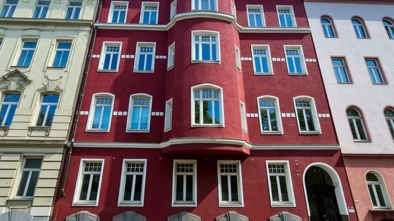 Rote Fassade eines Mehrfamilienhauses mit vielen Fenstern und architektonischen Details.