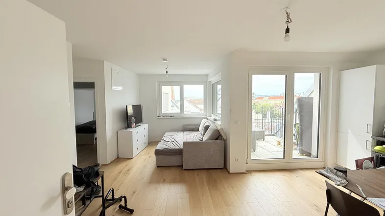 Helles Wohnzimmer mit Holzboden, Sofa und Zugang zu einem Außenbereich mit Stadtblick.