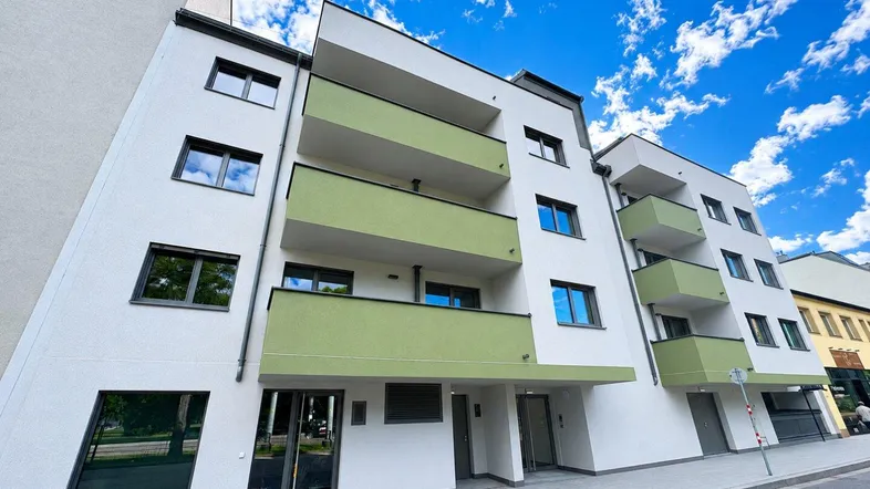 Moderne Wohnanlage mit weißer Fassade und grünen Balkonen unter blauem Himmel.