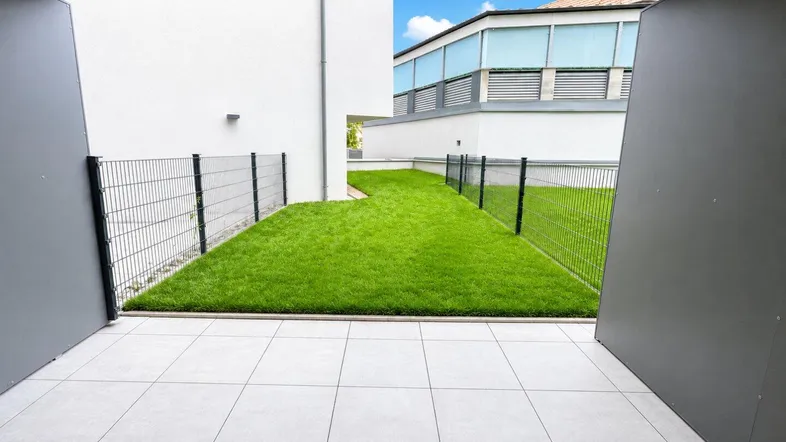 Geflieste Terrasse mit Zugang zu einem privaten Rasenbereich, umgeben von einem Zaun.