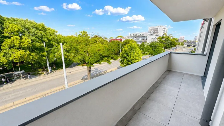 Geräumiger Balkon mit Fliesenboden und Blick auf die grüne Umgebung und die Straße.