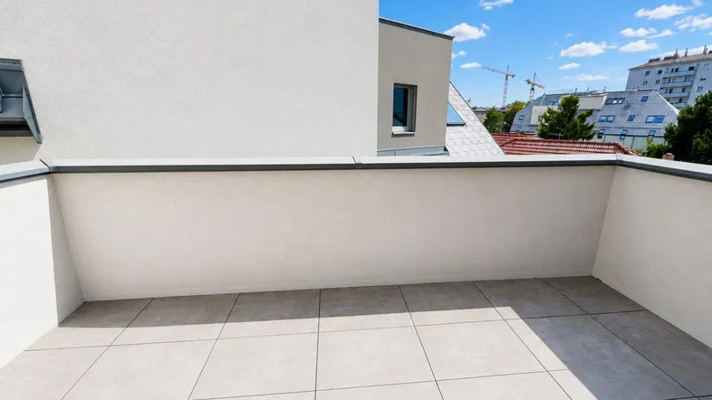 Geräumige, geflieste Terrasse mit Blick auf die umliegenden Gebäude und den blauen Himmel.