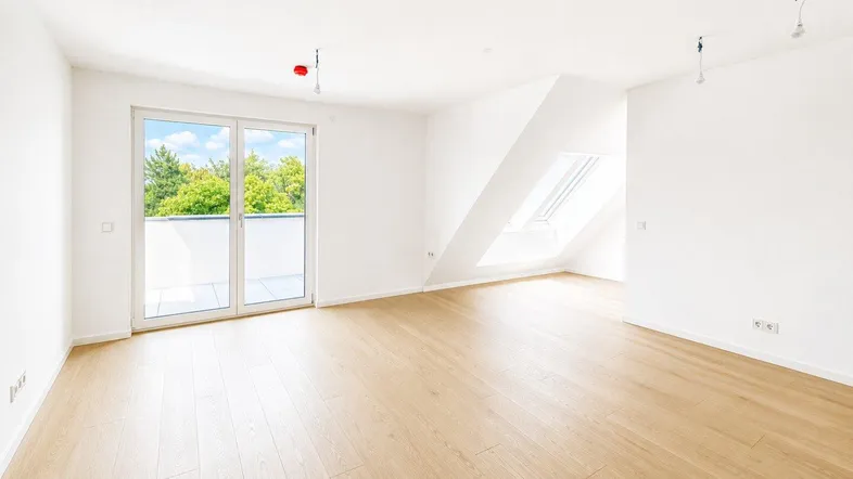 Helles, leeres Zimmer mit Holzboden, Zugang zum Balkon und Dachfenster in einem Neubau.