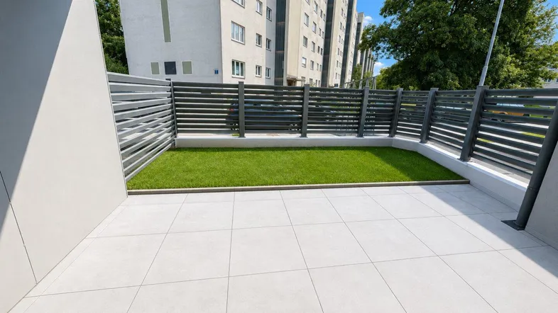 Geflieste Terrasse mit kleinem Rasenbereich und Blick auf das Wohngebäude.