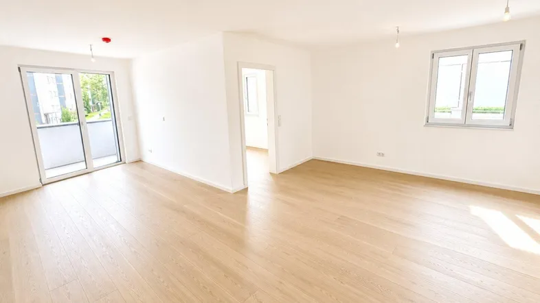 Helles und geräumiges Wohnzimmer mit modernem Parkettboden und Zugang zu einem Balkon.