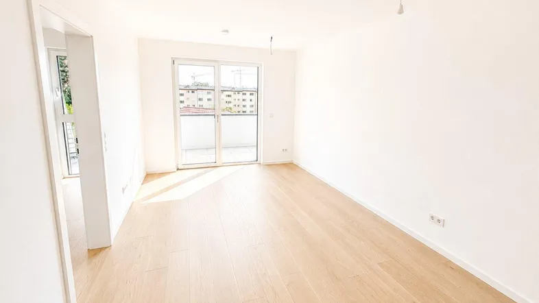 Helles, leeres Wohnzimmer mit neuem Parkettboden und Zugang zu einem Balkon.