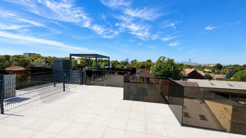 Große Dachterrasse mit Fliesenboden und weitem Blick über die Umgebung unter blauem Himmel.