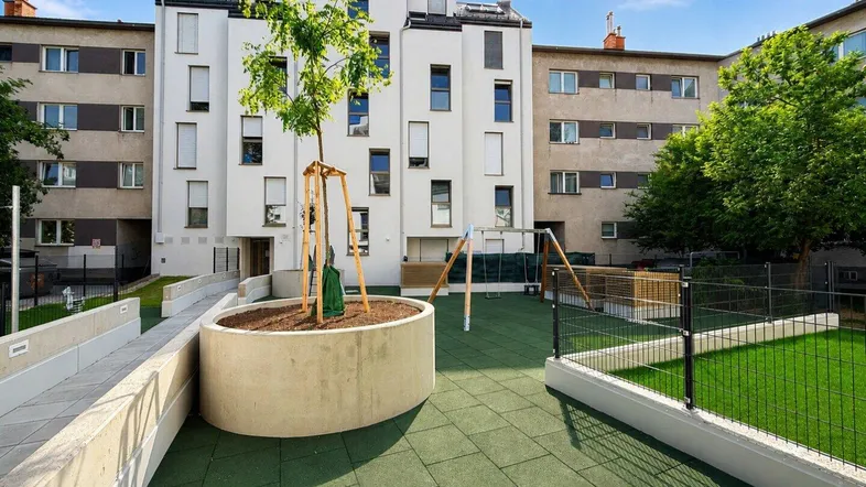 Spielplatzbereich mit modernen Wohngebäuden im Hintergrund unter blauem Himmel.