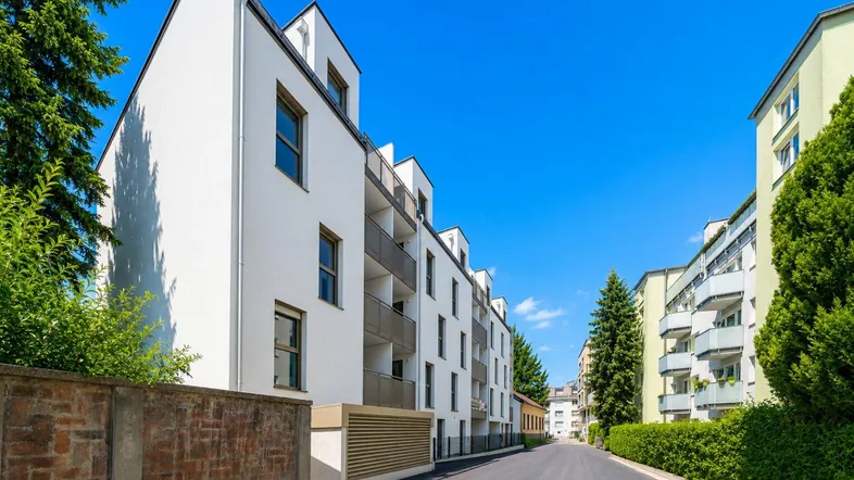 Modernes Mehrfamilienhaus mit weißer Fassade und Balkonen an einer ruhigen Wohnstraße.