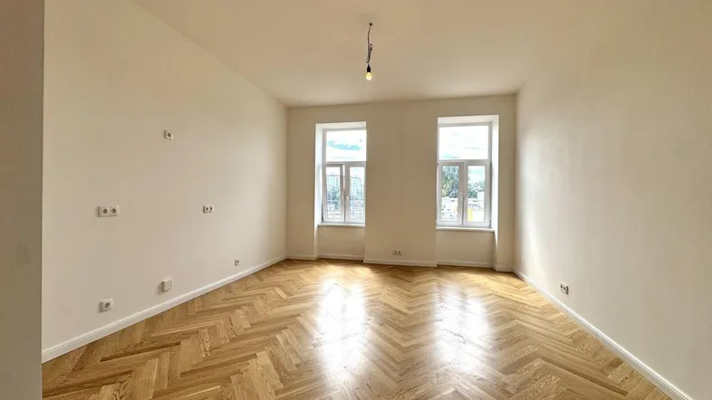 Helles, frisch renoviertes Zimmer mit Fischgrätparkett und hohen Decken, ideal als Wohnzimmer.