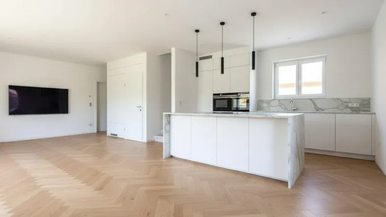 Helles, offenes Wohnzimmer mit moderner Küche, Kochinsel und Fischgrätparkettboden.