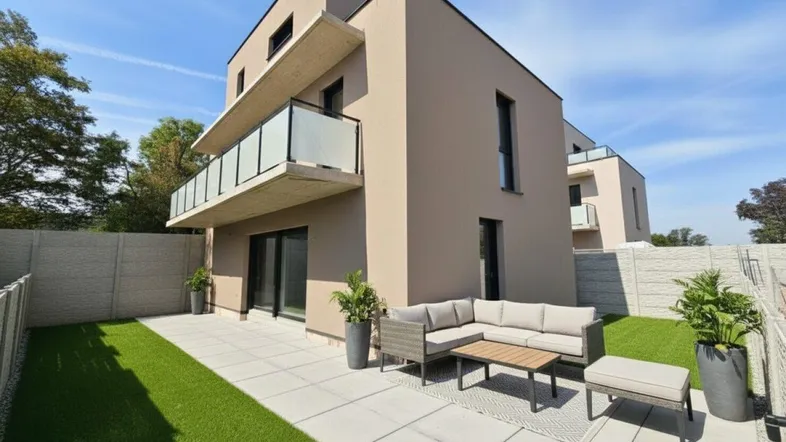 Moderne Hausfassade mit möblierter Terrasse und kleinem Rasenbereich unter blauem Himmel.
