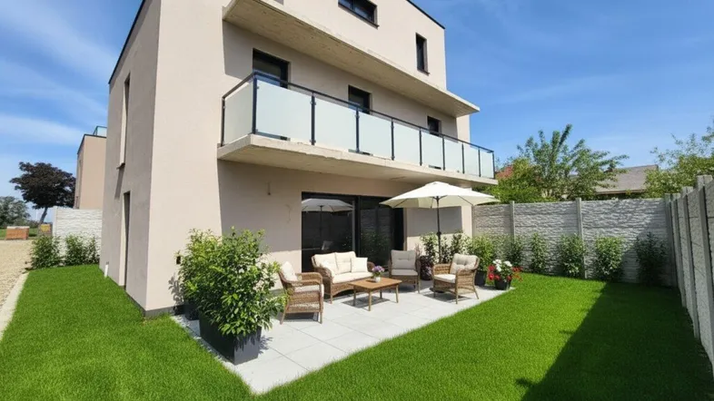 Moderne Doppelhaushälfte mit gepflegtem Garten und möblierter Terrasse unter blauem Himmel.