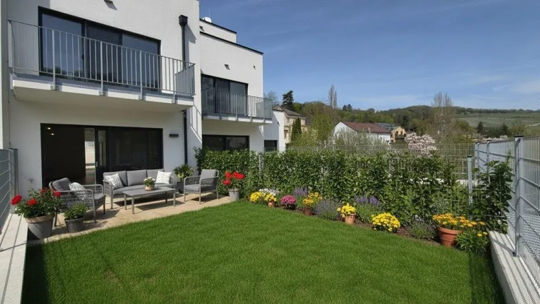 Gepflegter Gartenbereich mit Rasenfläche und möblierter Terrasse vor einem modernen Neubau.