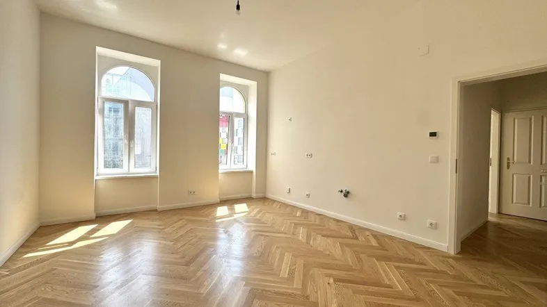 Heller Raum mit elegantem Fischgrätparkett, weißen Wänden und hohen Fenstern, die viel Tageslicht hereinlassen.