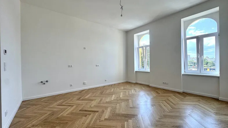 Helles, leeres Wohnzimmer mit Fischgrätparkett und hohen Bogenfenstern.