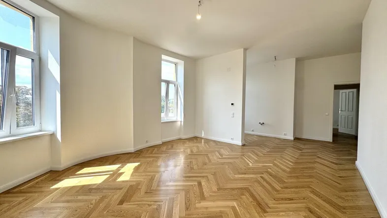 Helles, frisch renoviertes Wohnzimmer mit Fischgrätparkett und hohen Fenstern, die viel Tageslicht hereinlassen.