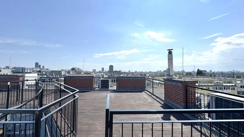 Dachterrasse mit weitem Blick über die Stadt und umliegende Gebäude unter blauem Himmel.