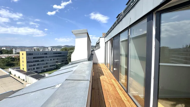 Geräumige Dachterrasse mit Holzboden und weitem Blick über die Stadt, zugänglich durch große Glasfronten.