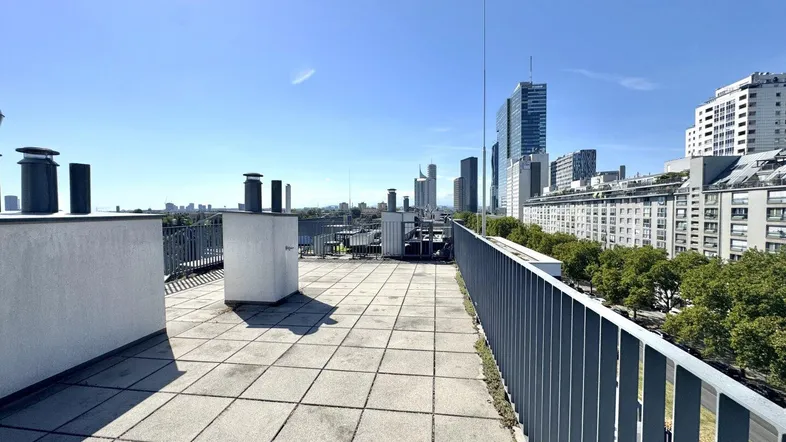Geräumige Dachterrasse mit Fliesenboden und weitem Blick auf die Stadt und moderne Hochhäuser.