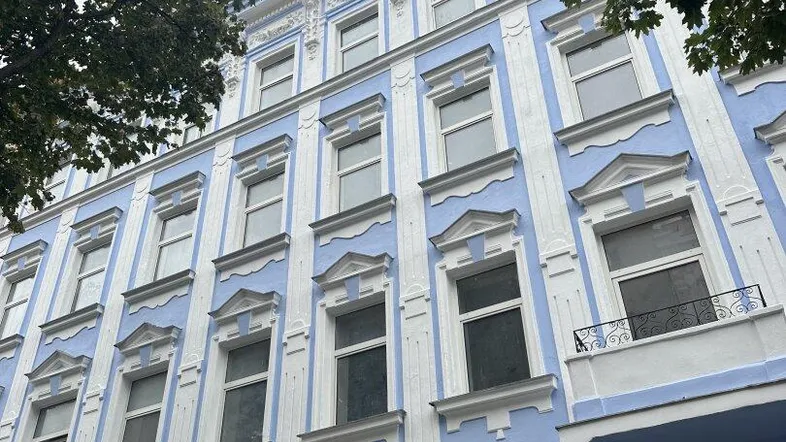 Historisches Gebäude mit hellblauer Fassade und weißen Stuckelementen unter bewölktem Himmel.