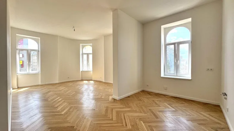 Helles, geräumiges Zimmer mit Fischgrätparkett und hohen Bogenfenstern, ideal als Wohnbereich.