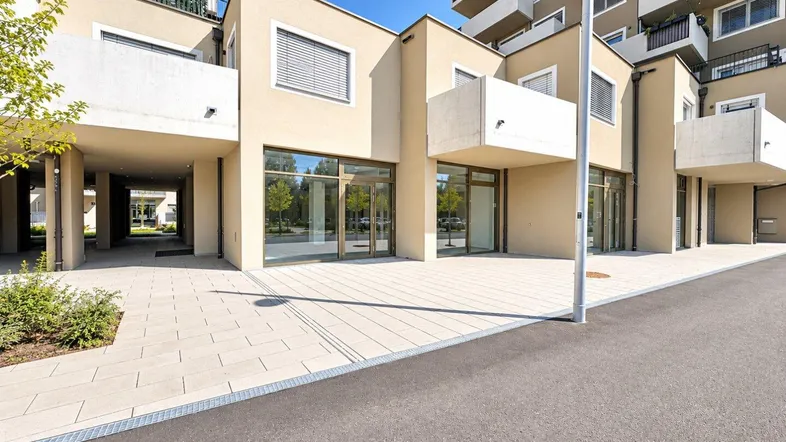 Moderne Geschäftsräume im Erdgeschoss eines Neubaus mit großen Schaufenstern und gepflastertem Vorplatz.