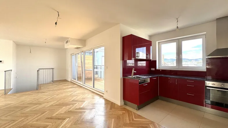 Heller offener Wohnbereich mit roter Einbauküche und Fischgrätparkettboden, mit Zugang zur Terrasse.